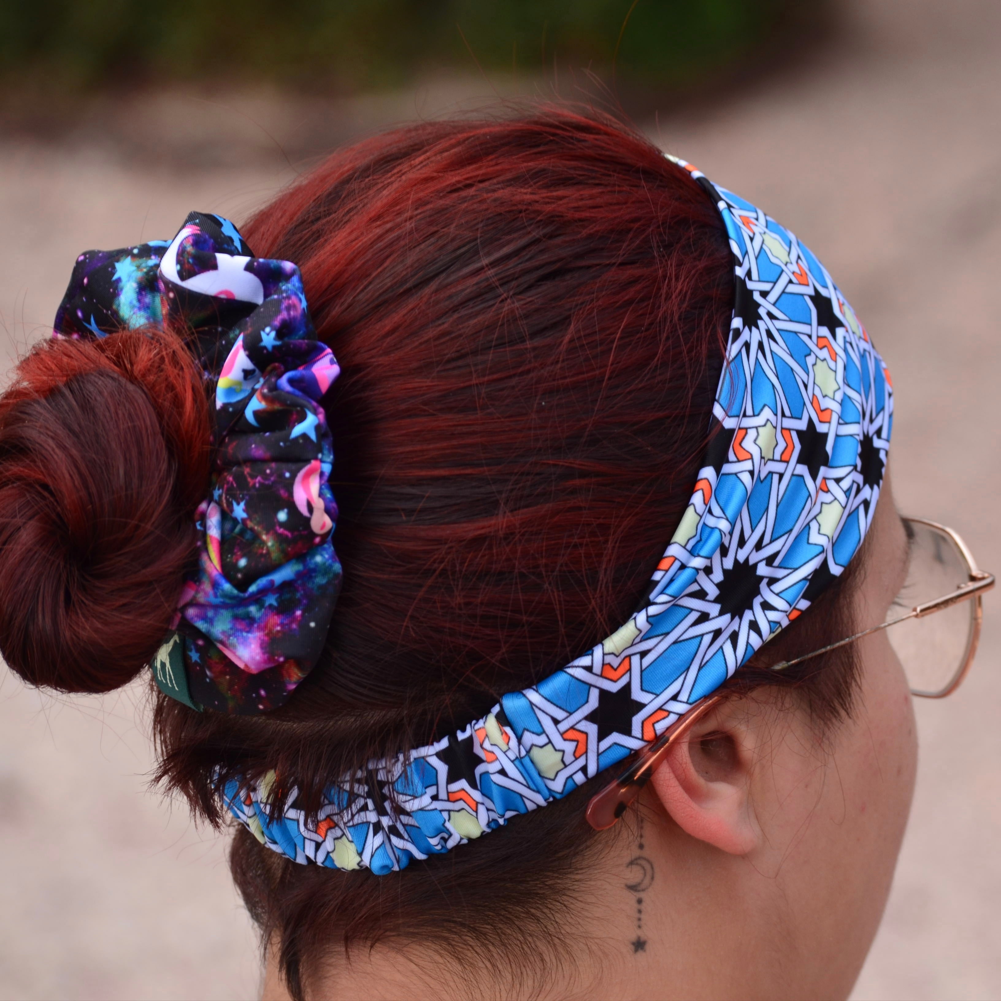 A close-up lifestyle shot of a person wearing a blue and white geometric patterned headband and matching scrunchie, with their reddish-brown hair styled in a bun.