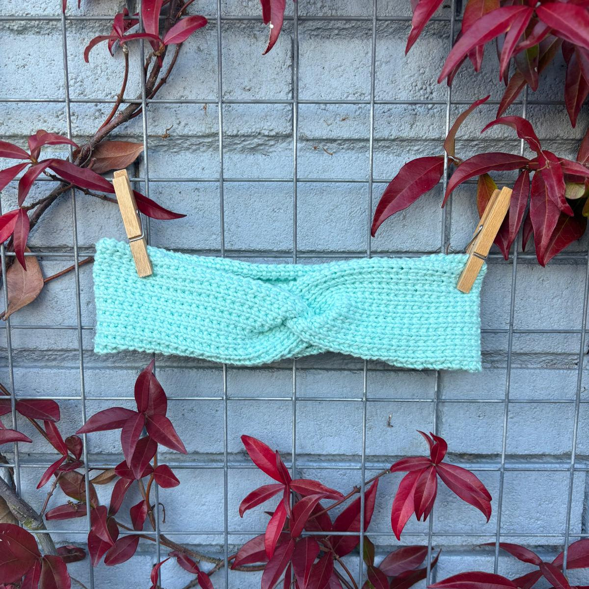 Turquoise knitted headband on a wire rack with red leaves around