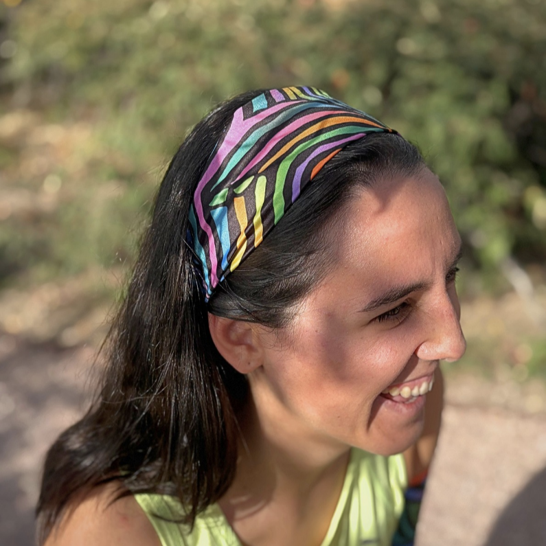 Woman wearing a colorful headband outdoors with greenery in the background